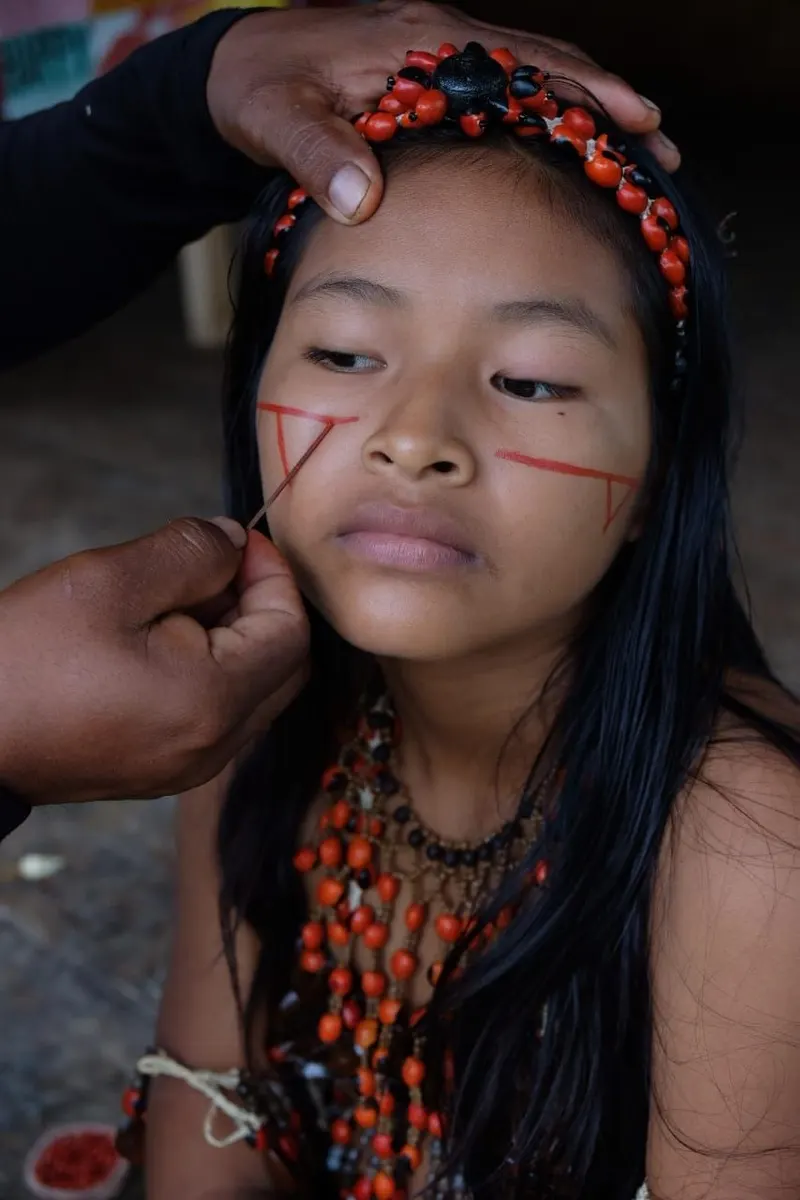 Retrato de una niña kichwa mientras le trazan con achiote el diseño ritual en el rostro